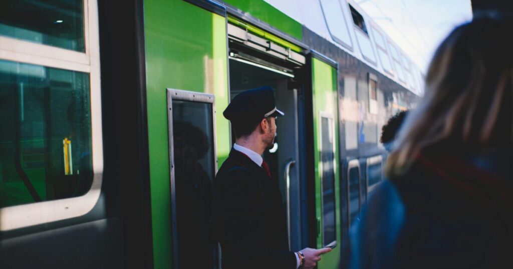 A train conductor at the entrance of a green train in Venice, Italy. Daytime scene with passengers.